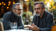 © Nature_Beauty - Two men with graying hair and glasses sit at a table, engaged in conversation