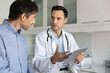 © fizkes - Serious doctor talking to male patient, showing examination results on tablet, explaining diagnosis, treatment recommendation, giving consultation in hospital checkup room