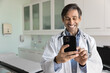 © fizkes - Cheerful male Hispanic doctor man chatting with patients on mobile phone, browsing Internet, using modern technology, medical app on smartphone, typing, smiling, laughing