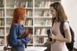 © fizkes - Students everyday life. Two happy stylish looking teen girls friends of different ethnic groups meet at college university library take break in learning routine enjoy chatting talk share school news