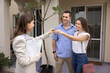 © fizkes - Happy young couple getting key from real estate agent, broker, ready to move into new rental, accommodation, bought house, meeting with realtor woman at entrance, talking, laughing