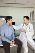 © fizkes - Positive male doctor explaining diagnosis to friend patient, touching mans shoulder with support, talking, telling successful therapy details, treatment recommendations, sitting on hospital couch