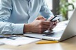 © PlanetOfVectors - Close-up of a person using a smartphone at a desk with a laptop and documents, bright modern office, concept of multitasking and communication. Ai generative