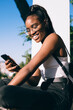 © BullRun - Smiling African American woman using smartphone on balcony in park