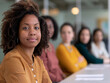 © Artinun - Young woman with curly hair focusing on camera in a diverse group of people seated at a conference table during a professional meeting in a modern office