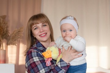 Happy, cheerful ukrainian mother holds a laughing baby daughter in her arms. Concept of motherhood and a loving family