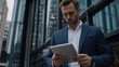 © WS Studio 1985 - Focused Businessman: A serious businessman reviews data on his tablet outside a modern office building.  The image conveys professionalism, concentration.