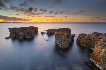 Wall Mural - Beautiful nature seascape of beach shore among rocks on evening sunset.