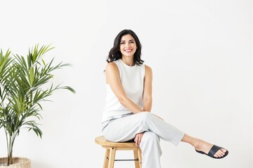 Wall Mural - Woman sitting on a wooden stool beside a potted plant.