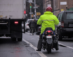 Motorcycle rider dressed in yellow rain jacket riding in bicycle lane in Brooklyn, New York City.