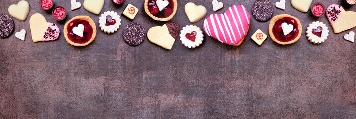 Wall Mural - Valentines Day baking and sweets top border with a variety of cookies, chocolates and sweet treats. Top down view on a dark stone banner background with copy space. Love and hearts theme.