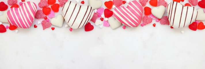 Aufkleber - Valentines Day heart shaped sweets top border with donuts and candies. Overhead view on a white marble banner background with copy space.