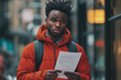 © Kieran - Man in a red hoodie holding a letter while standing in an urban street