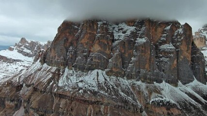 Wall Mural - aerial view of amazing rocky mountains in snow under moody gray clouds, dolomites, italy, 4k