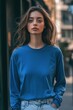 © Aleksander - A young woman with long hair wearing a blue long sleeve T-shirt mockup, standing outdoors in a city setting. She has a neutral expression and is looking directly at the camera.