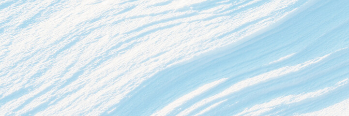 Wall Mural - Wide panoramic winter background with snowy ground. Natural snow texture. Wind sculpted patterns on snow surface.