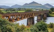 © alisya - Scenic rusty bridge spans river, mountains backdrop; travel, landscape