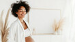 © Top AI images - Pregnant woman with afro hairstyle smiling softly indoors, copy space