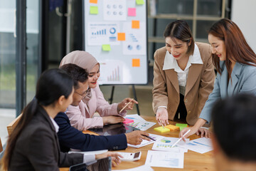 Sticker - Group of asian professionals collaborating and working together in a  office. They are discussing project solutions and working on paperwork. The team looks happy, successful.
