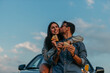 © La Famiglia - Couple sharing pizza while leaning on a car and taking a selfies during a picturesque sunset
