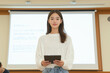 © Александра Ходорковс - Asian young woman presenting with tablet in classroom setting