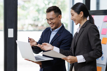 Asian businessman and businesswoman looking at laptop computer in the workplace office, Feeling happiness
