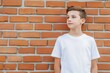 © Sebelas Studio - A young boy in a white t-shirt stands against a brick wall.