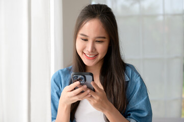 Wall Mural - Young Asian woman enjoy using smartphone at home