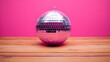 © Tark - Pink disco ball on wooden table and pink background. Generative AI