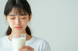 © smth.design - Asian young woman holding a glass of milk with eyes closed in serene, minimalistic setting