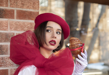 beautiful woman with red beret and big ribbon on shoulder drinking coffee or cappuccino in cafe and eating croissant.girl posing for french pastry