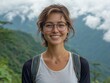 © Ilie - Young woman with glasses smiling amidst scenic mountain backdrop, exuding joy and adventure.