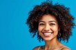 © mamo studios - Feeling good in blue. Happy woman with curly hair smiling at the camera while standing against a blue background. Beautiful woman with curly hair wearing her natural air with pride.