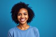 © mamo studios - Feeling good in blue. Happy woman with curly hair smiling at the camera while standing against a blue background. Beautiful woman with curly hair wearing her natural air with pride.