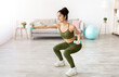 © Prostock-studio - Happy young Indian woman doing squats with dumbbells at home, full length. Positive millennial Asian lady performing strength exercises, keeping in good shape during covid quarantine