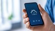 © khonkangrua - Hand Holding Smartphone with Home Automation App on Screen Showing House Icon and Various Controls