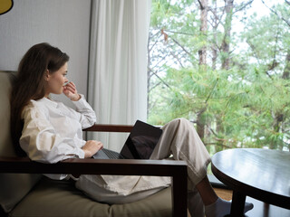 Canvas Print - Young woman in casual attire contemplating while sitting in a cozy chair by the window, expressing tranquility and focus in a natural setting