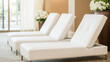 © pattozher - Serene Spa Lounge: Three pristine white chaise lounges beckon relaxation in a tranquil spa setting.  Sunlight streams through a nearby window, enhancing the atmosphere of serenity and calm.