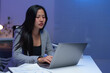 © Phimwilai - Young asian businesswoman concentrating on her work on a laptop in a modern office, working late at night with a focused expression, demonstrating dedication and professionalism