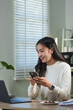 © crizzystudio - Happy businesswoman using smartphone while working remotely from home, enjoying online communication, browsing internet, using mobile app, shopping online, checking social media or texting message