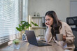 © crizzystudio - Young asian businesswoman working from home office and having problems, looking worried at laptop screen while drinking coffee, with plants and blinds in the background