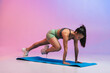 © Westend61 - Young woman exercising on yoga mat against colored background