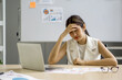 © chadchai - Young asian businesswoman hold her temple, sitting in the office. The concept of unemployed, sadness, depressed and human problem.
