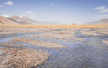 Wall Mural - High-mountain river flows in a valley against the background of rocky mountain ranges in the Tien Shan mountains in the Pamirs in Tajikistan, landscape for background