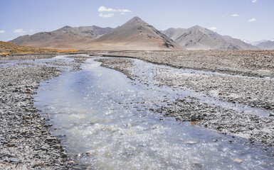 Wall Mural - High-mountain river flows in a valley against the background of rocky mountain ranges in the Tien Shan mountains in the Pamirs in Tajikistan, landscape for background