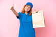© luismolinero - Young caucasian woman taking a bag of takeaway food isolated on pink background giving a thumbs up gesture