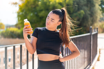 Wall Mural - Young pretty sport woman holding an orange juice at outdoors with sad expression