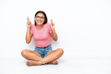 Wall Mural - Young caucasian woman sitting on the floor isolated on white background with fingers crossing