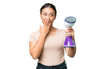 Young Uruguayan woman holding a vertical steam iron over isolated chroma key background with surprise and shocked facial expression