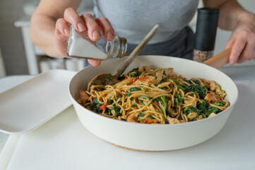 Wall Mural - Woman in the kitchen with a fresh cooked and healthy meal with whole wheat pasta, vegetables and meat in a skillet